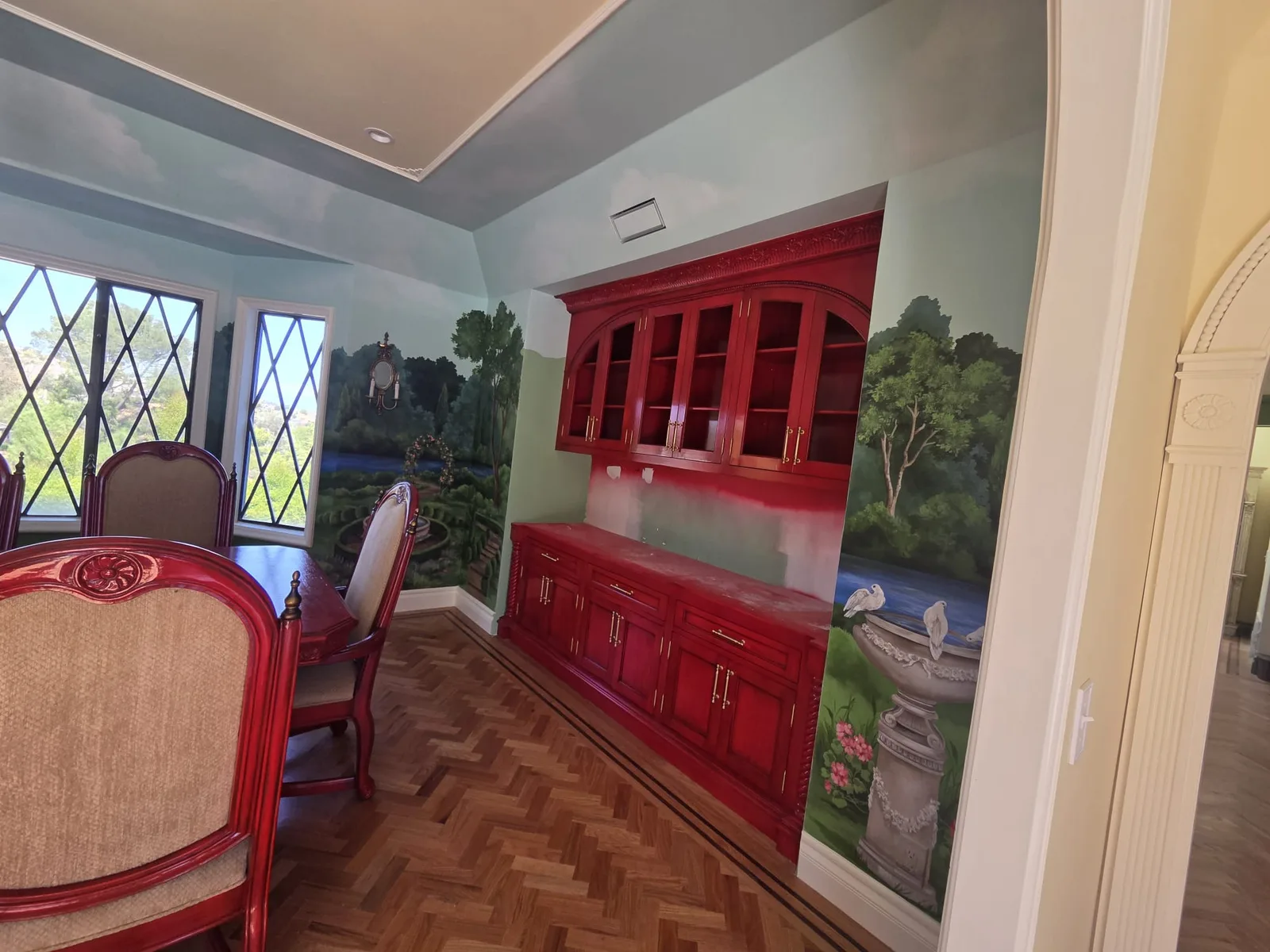 Dining room with a hand-painted garden mural surrounding a lacquered cabinet.